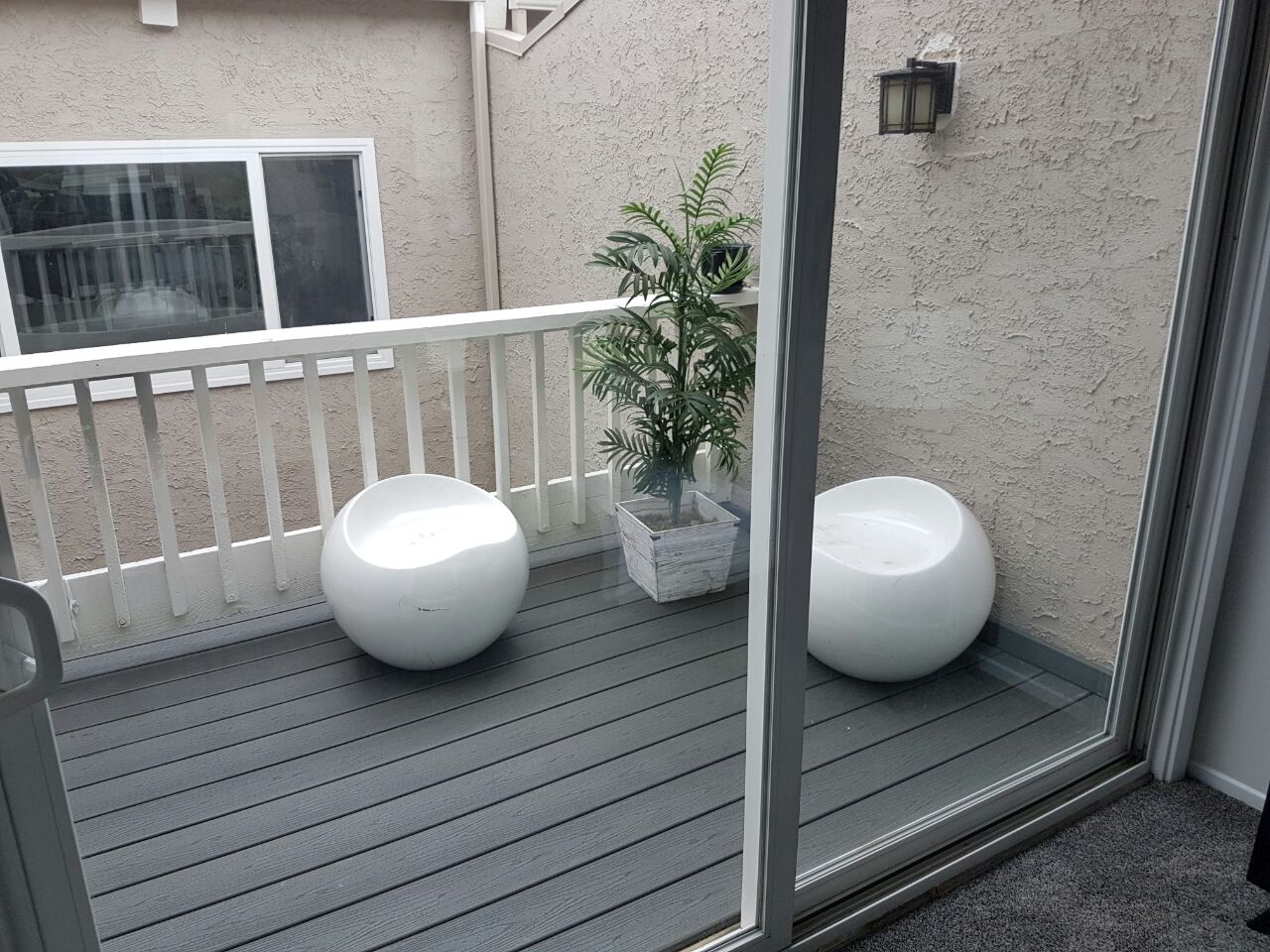 A balcony with two white chairs and potted plant.